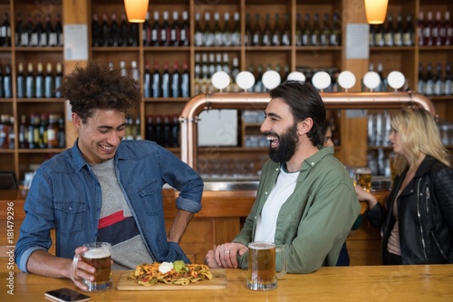 Two male friends having glass of beer and mexican food in bar