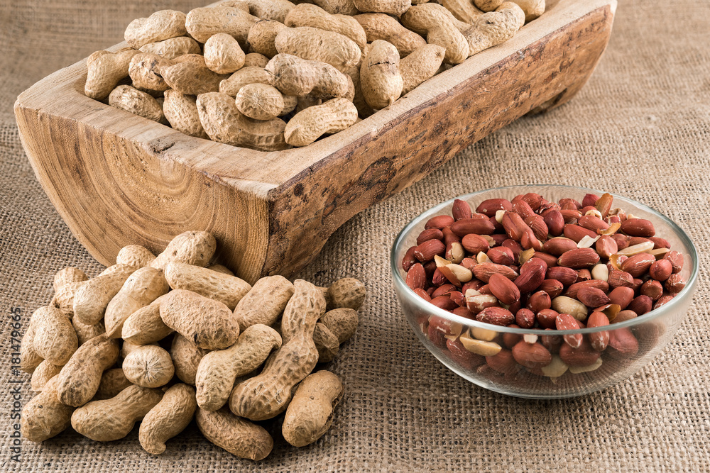 Peanuts in nutshell on a piece of wood and peeled peanuts in a bowl on sackcloth Peanuts in nutshell on a piece of wood and peeled peanuts in a bowl on sackcloth