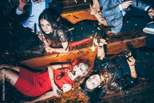 Beautiful young women having fun on crazy party lying on the floor in confetti