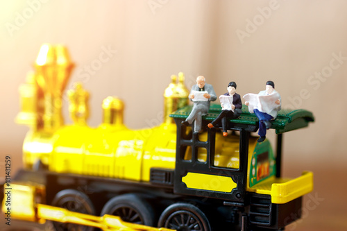 Miniature people reading and sitting on yellow train, education or business concept.
