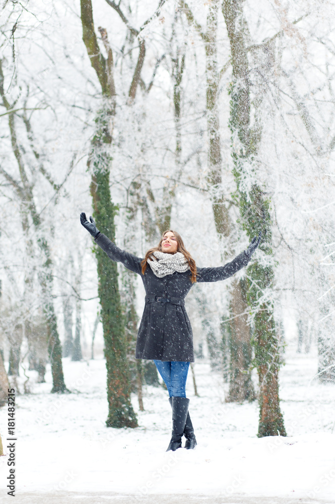 Winter portrait of beautiful young woman in park with open arms.