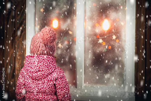 On Christmas night an adorable little girl near the window the snow falls.