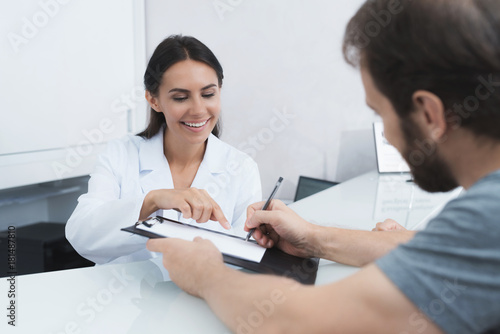 The secretary in a medical clinic helps the patient complete the necessary forms before starting treatment.