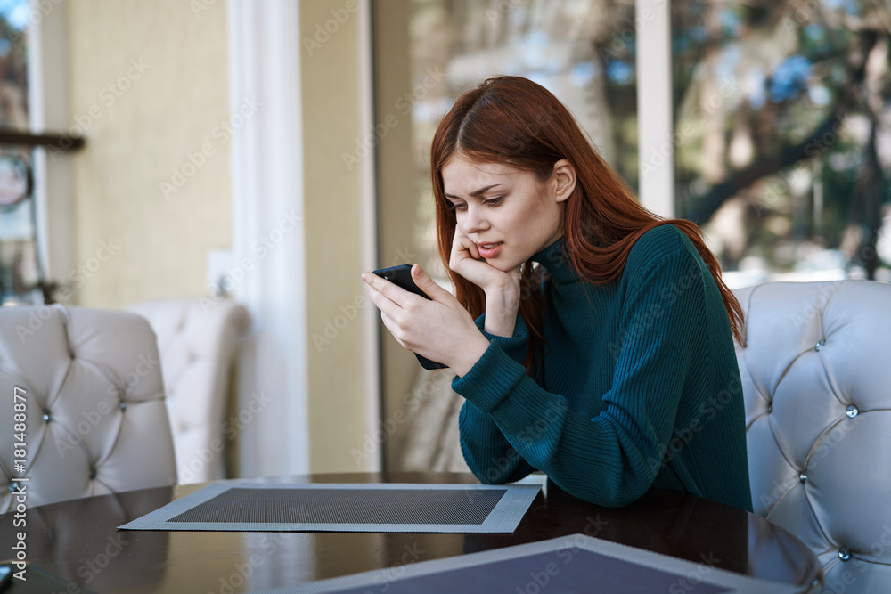 Beautiful young woman with phone in hands sits in cafe on the street in the autumn Beautiful young woman with phone in hands sits in cafe on the street in the autumn