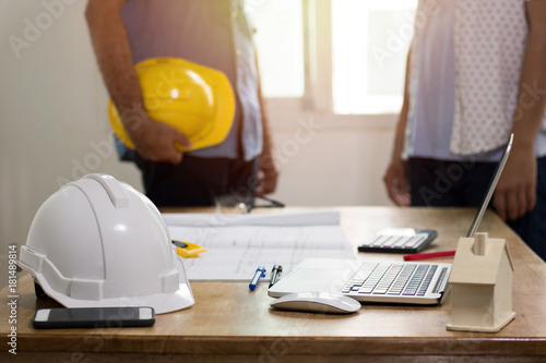 focus at safty helmet on working desk and two engineer standing and dicuss background . photo