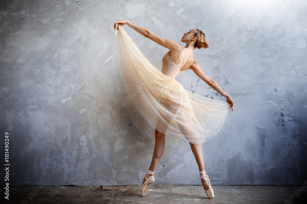 Naklejka premium Young ballerina in a golden colored dancing costume is posing in a loft studio