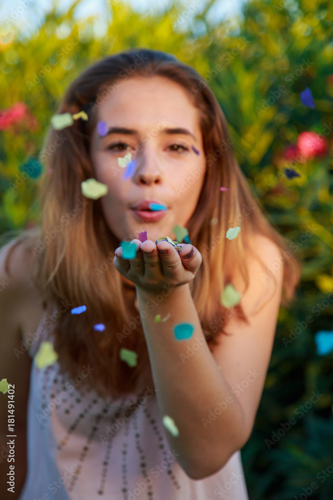 Pretty young woman standing in park on sunset and blowing confetti. Pretty young woman standing in park on sunset and blowing confetti.