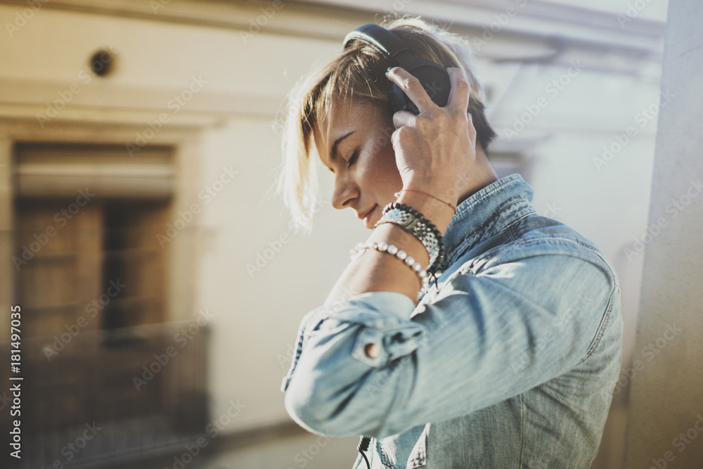 Fototapeta premium Smiling beautiful girl relaxing at home,wearing casual clothes,playing music,using smartphone and listening audio books in modern headphones.Young pretty woman music lover at room.Blurred background.