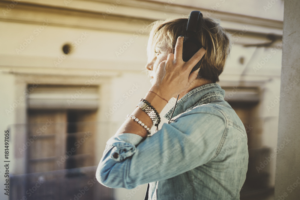 Smiling beautiful girl relaxing at home,wearing casual clothes,playing music,using smartphone and listening audio books in modern headphones.Young pretty woman music lover at room.Blurred background.