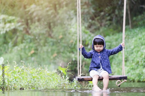Little cute girl child on swing above the river. She is feeling lonely and chill.