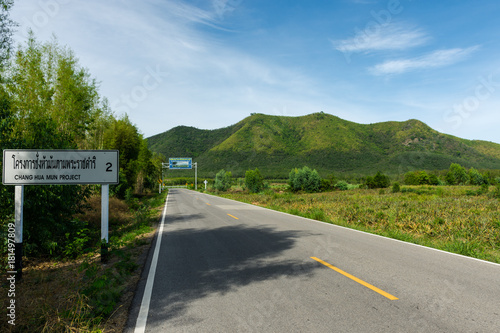 The route of road go to “Chang Hua Mun Project” with mountain, trees, sky views and sign in Thai word mean Chang Hua Mun Project at Phetchaburi province, Thailand