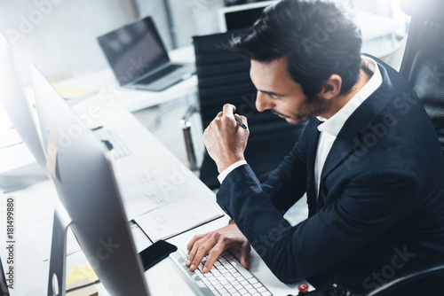 Confident man in formal wear thinking and working with desktop computer at modern lightful office.Horizontal.Blurred background. photo