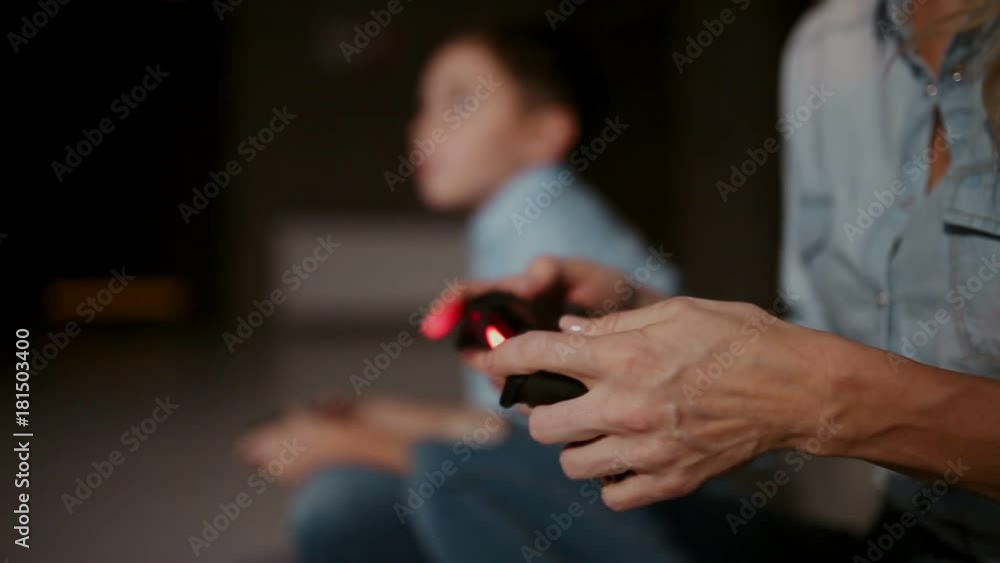 Hands holding a controller to a game console, and in the background the boy looks at the faucet and playing video games. The focus shifts from one to another. Hands holding a controller to a game console, and in the background the boy looks at the faucet and playing video games. The focus shifts from one to another.