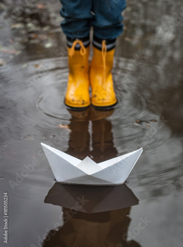 Child with Yellow Rain Boots and a little White Paper boat / Ship: Playing in a puddle, imagining his adventures photo