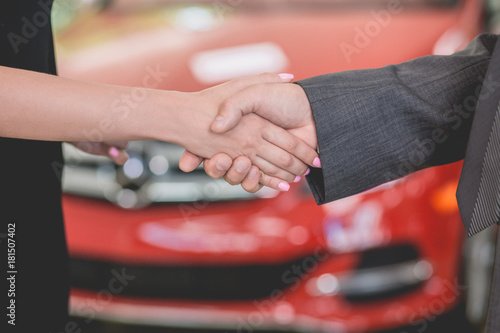 Vehicle dealer shaking hand with young woman. New owner of electro car.