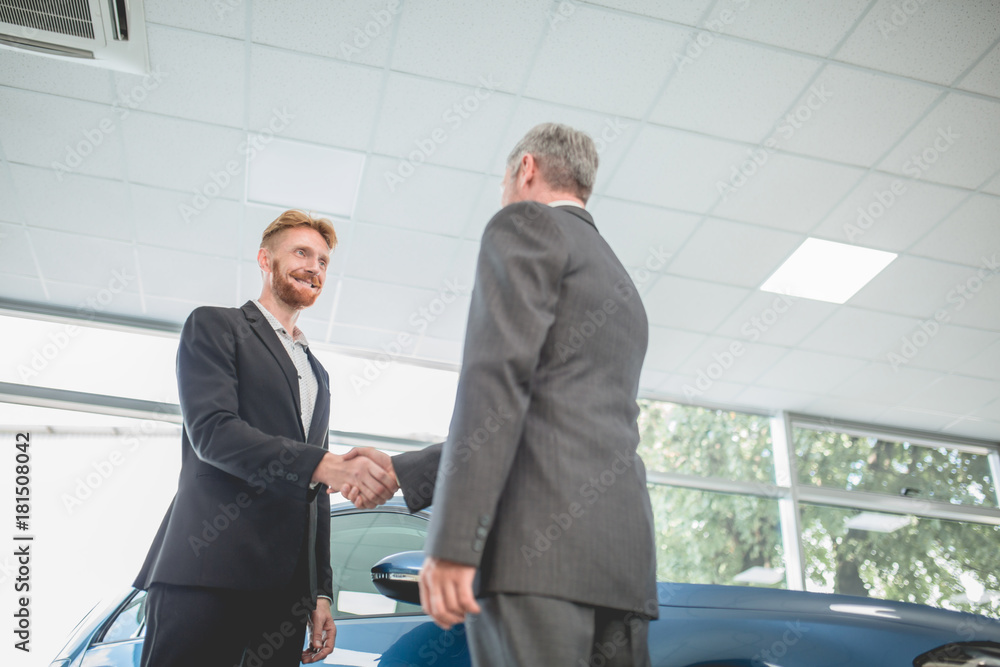 Handsome man shaking hand with vehicle seller. Car showroom, man purchasing new car. Handsome man shaking hand with vehicle seller. Car showroom, man purchasing new car.