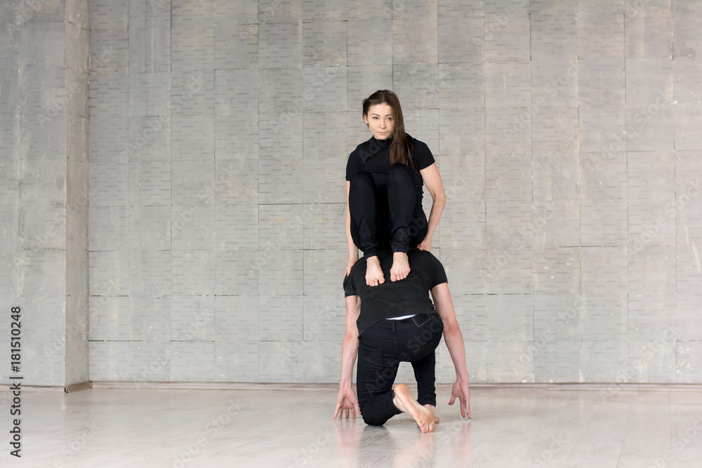 Beautiful couple practising dance elements. Young woman sitting on boys back over grey background, they are dancing. Element of modern dance.