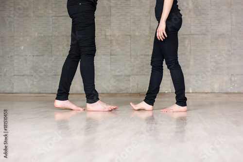 Education of modern dance. Young boy and girl in black clothing standing with bare feet on grey background. School of modern dance.