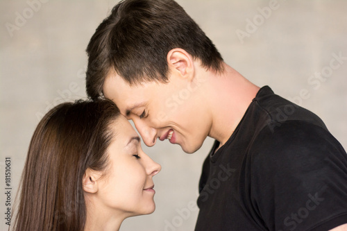 Portrait of two lovers, grey background. Couple of youg loving people enjoying of each other close up.
