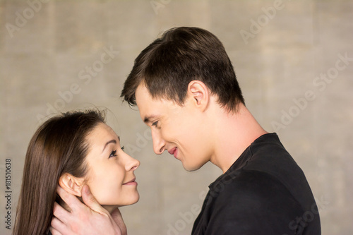 Young couple hugging on grey background. Portrait of beuautiful young man and woman looking at each other in embrace. Love and romance concept.