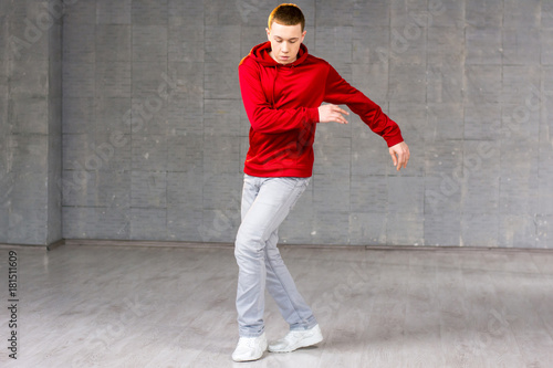 Young male modern dancer dancing. Modern style dancer in red sweater dancing brake dance over grey background. Young talented freestyle dancer.