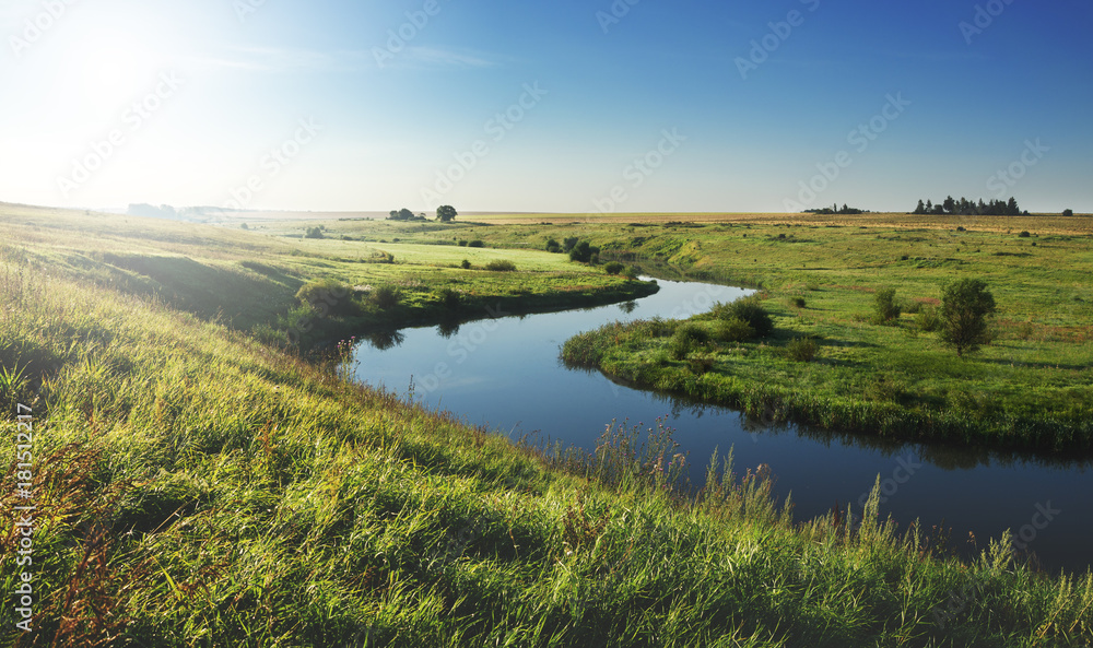 Sunny summer landscape with river.Green meadows and fields at sunrise.