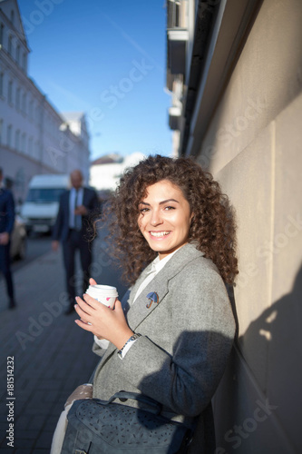 the girl walks the streets of Europe. brunette with curly hair on the background of passing men. Coffee pause . Life in the city .