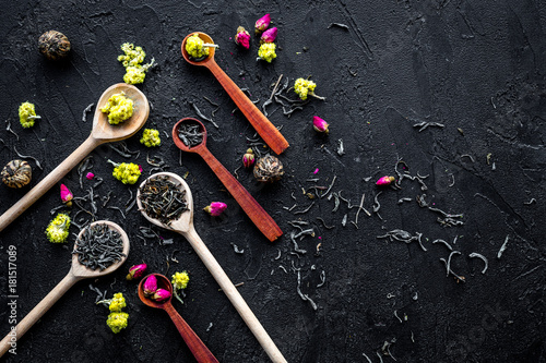 Aromatic tea. Wooden spoons with dried tea leaves, flowers and spices on black background top view copyspace
