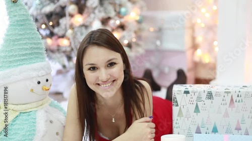 Happy joyful girl lying down looking at camera among New Year's gifts in festive interior photo