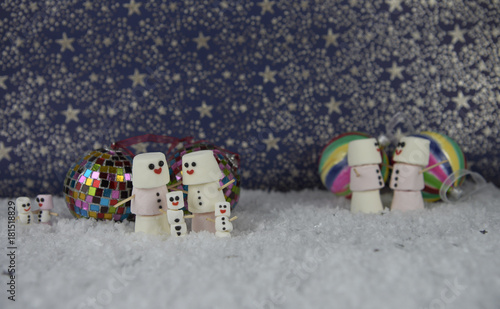 Christmas photography image of marshmallows shaped as snowman with tree decoration baubles on star pattern background and snow base