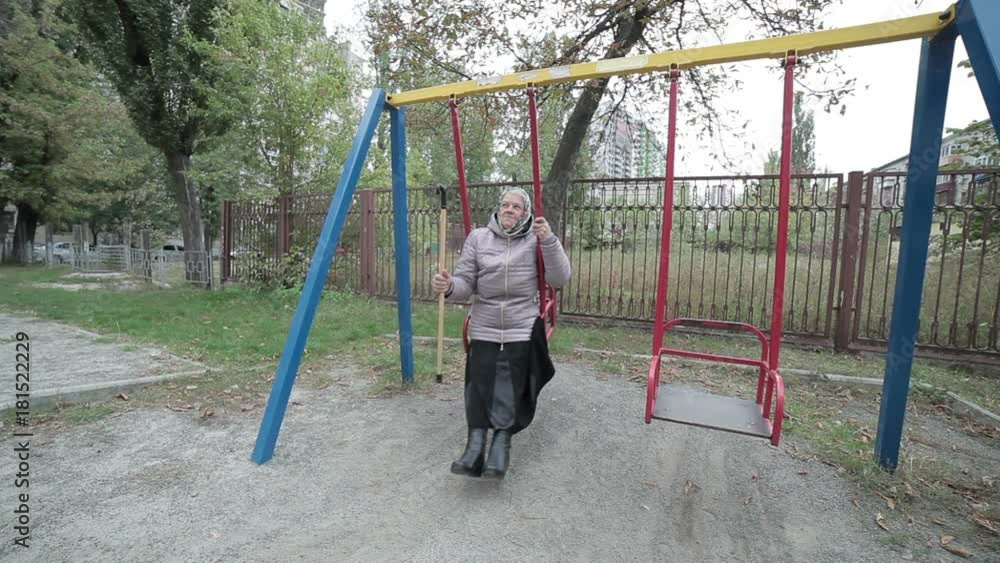 Old woman is swinging on a swing for the children, in her hand she is holding a wand for the elderly. Old woman is swinging on a swing for the children, in her hand she is holding a wand for the elderly.