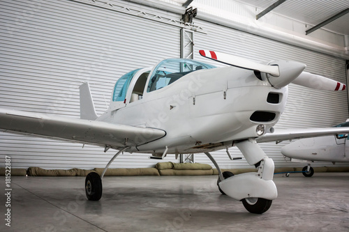 Small sports airplane with opened cockpit canopy in the hangar
