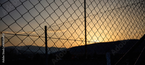 Steel wire mesh fence on a sunset background. Blurred city and hills silhouette.