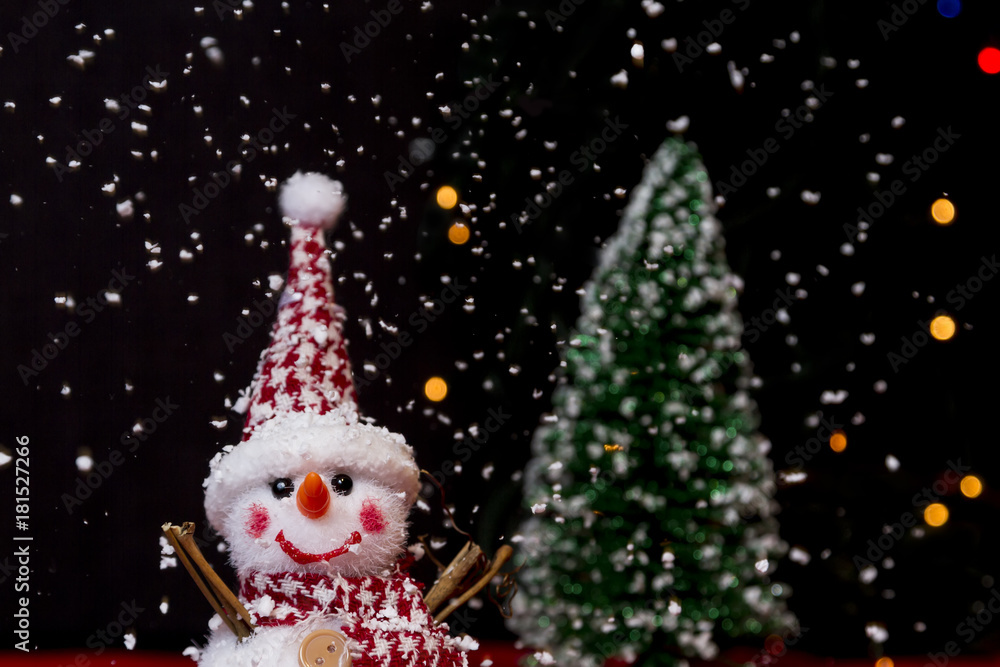 Snowman on snow over blurred christmas tree and light bokeh