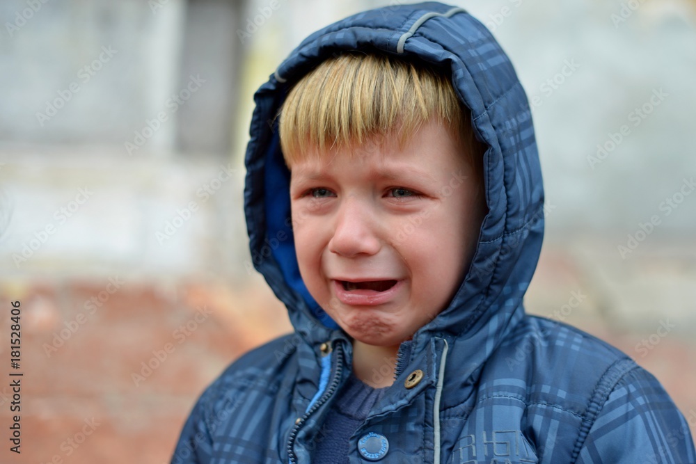 A boy in a blue jacket in a hood, crying with tears