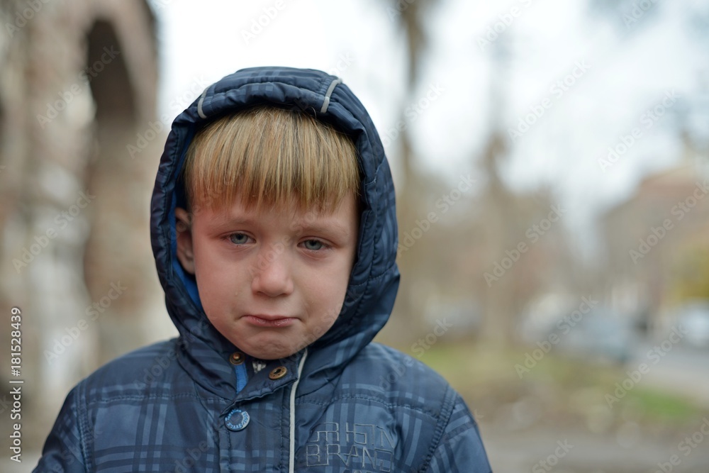 A boy in a blue jacket in a hood, crying with tears A boy in a blue jacket in a hood, crying with tears