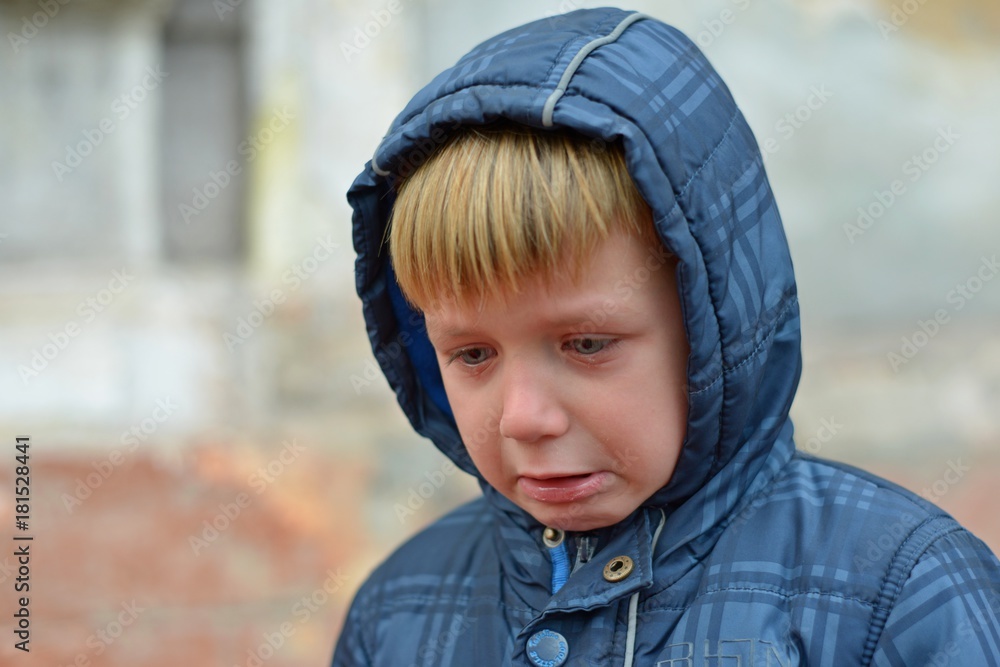 A boy in a blue jacket in a hood, crying with tears A boy in a blue jacket in a hood, crying with tears