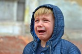 A boy in a blue jacket in a hood, crying with tears
