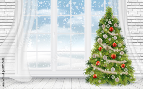 Decorated Christmas tree in the interior of a light living room on the background of a large window.