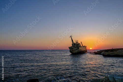 Sunset of shipwreck listing by rocks in the sea near Pafos, Cyprus.
