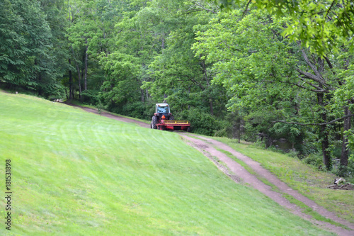 Farm Tractor Pulling Hay Disc Across Dirt Path on Country Farm