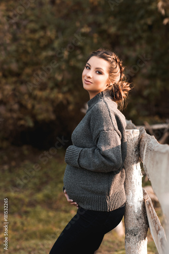 Pretty pregnant woman resting outdoors wearing cozy knitted sweater. Looking at camera. Maternity. Motherhood.