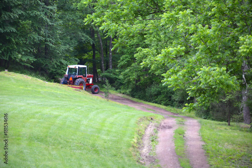 Farm Tractor Pulling Hay Disc Across Dirt Path on Country Farm
