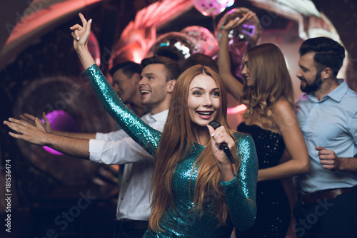 A woman in a green dress is singing songs with her friends at a karaoke club. Her friends have fun on the background.