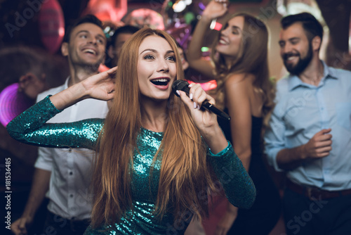 A woman in a green dress is singing songs with her friends at a karaoke club. Her friends have fun on the background.