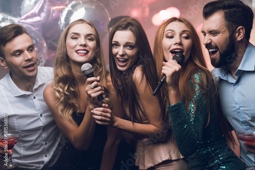 Three beautiful girls sing in a karaoke club. Behind them are men waiting for their turn. photo