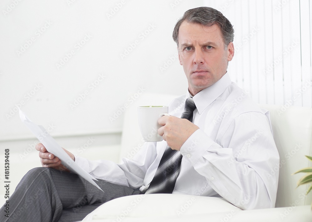 confident businessman drinking tea and reading a document,sitting in a chair in the hotel room confident businessman drinking tea and reading a document,sitting in a chair in the hotel room