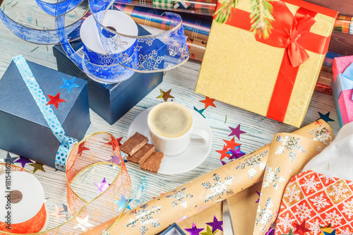 A package of Christmas gift box. Christmas christmas wrapping paper, ribbon, bow and string, scissors and coffee cup on a wooden background. Winter time new year photo