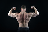 Athletic bodybuilder pose in pants isolated on black background.