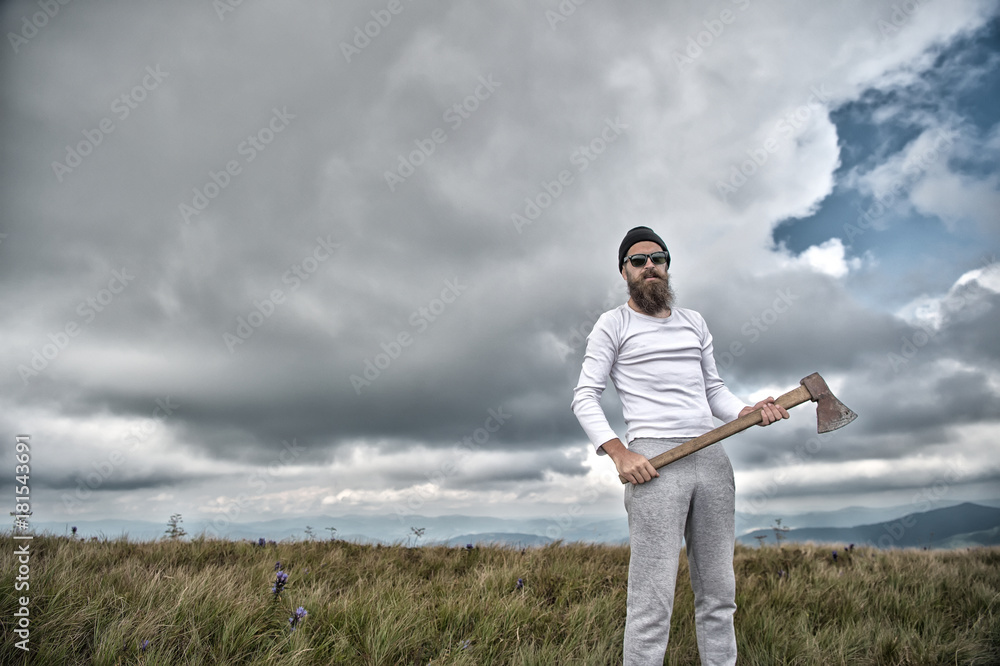 Hipster in sunglasses with axe stand on mountain landscape Hipster in sunglasses with axe stand on mountain landscape